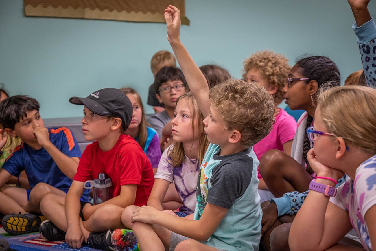Elementary students sitting on the floor listening to their teacher