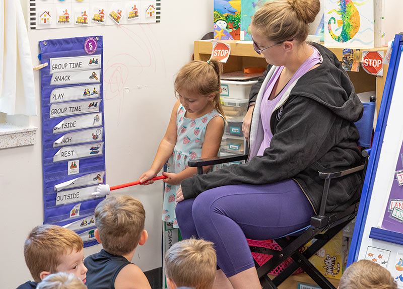 A student helping a teacher in front of the class