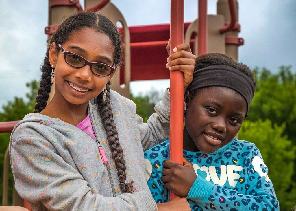 Two school age girls playing on the playground smiling at the camera