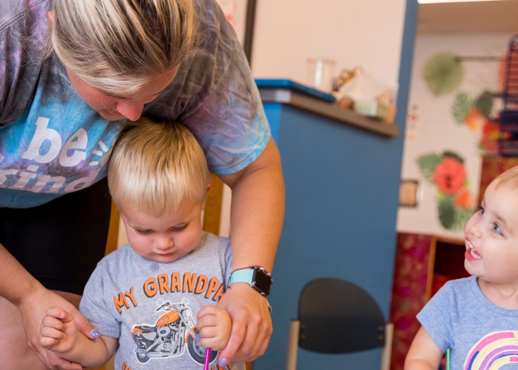 A teacher helping a toddler paint