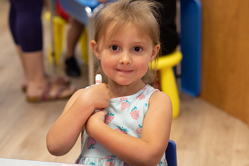 A child holding a marker smiling at the camera
